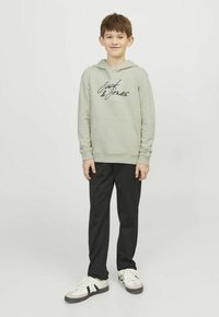 Felpa grigia chiara con tasca a kangaroo frontale, dotata di un logo nero; abbinata a pantaloni neri e sneaker bianche con dettagli grigi.
