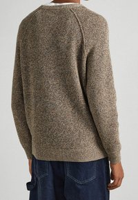 Maglione lavorato a maglia in tonalità marroni con una finitura texture. Caratterizzato da un collo rotondo e polsini a coste, mostra una vestibilità rilassata e maniche raglan.