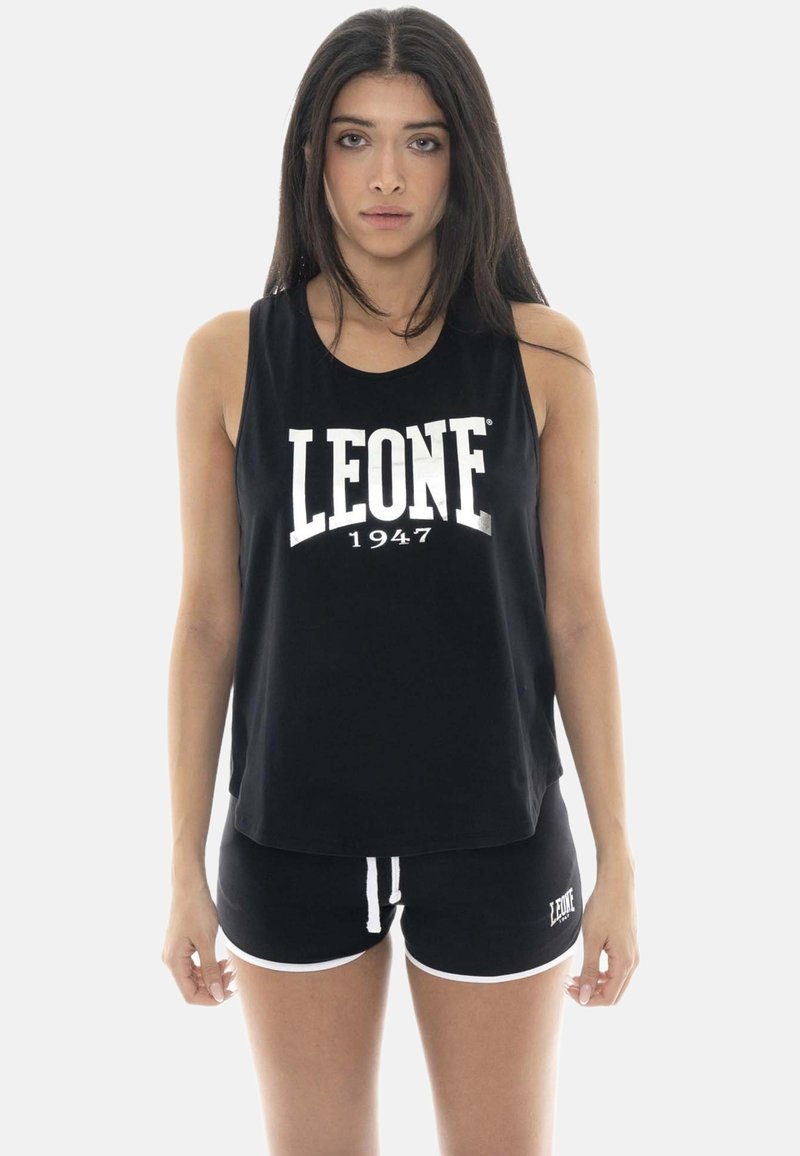 Jeune femme aux longs cheveux foncés portant un haut sans manches noir et un short assorti avec un texte blanc "LEONE 1947".