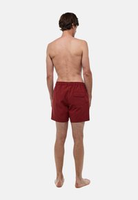 Shorts de bain à motifs rouges avec une taille élastique, une poche arrière et un tissu texturé, présentés de dos.