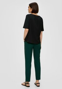 Zwart t-shirt met korte mouwen en een ronde halslijn, gecombineerd met groene rechte broek en platte zwarte sandaaltjes. Eenvoudig, strak ontwerp.