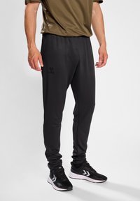 Schwarze Sporthose aus weichem Material, mit elastischem Bund und Taschen an den Seiten. Enthält ein dezentes Markenlogo am Oberschenkel.
