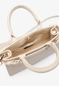 Beige håndveske laget av glatt syntetisk materiale, med doble topphåndtak, gullfargede detaljer og et romslig interiør med en liten lomme.
