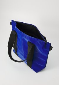 Kék vinil bevásárlótáska fekete textil fogantyúkkal, cipzáras tetejével és sima, fényes felületével. Belső része fekete béléssel van ellátva.