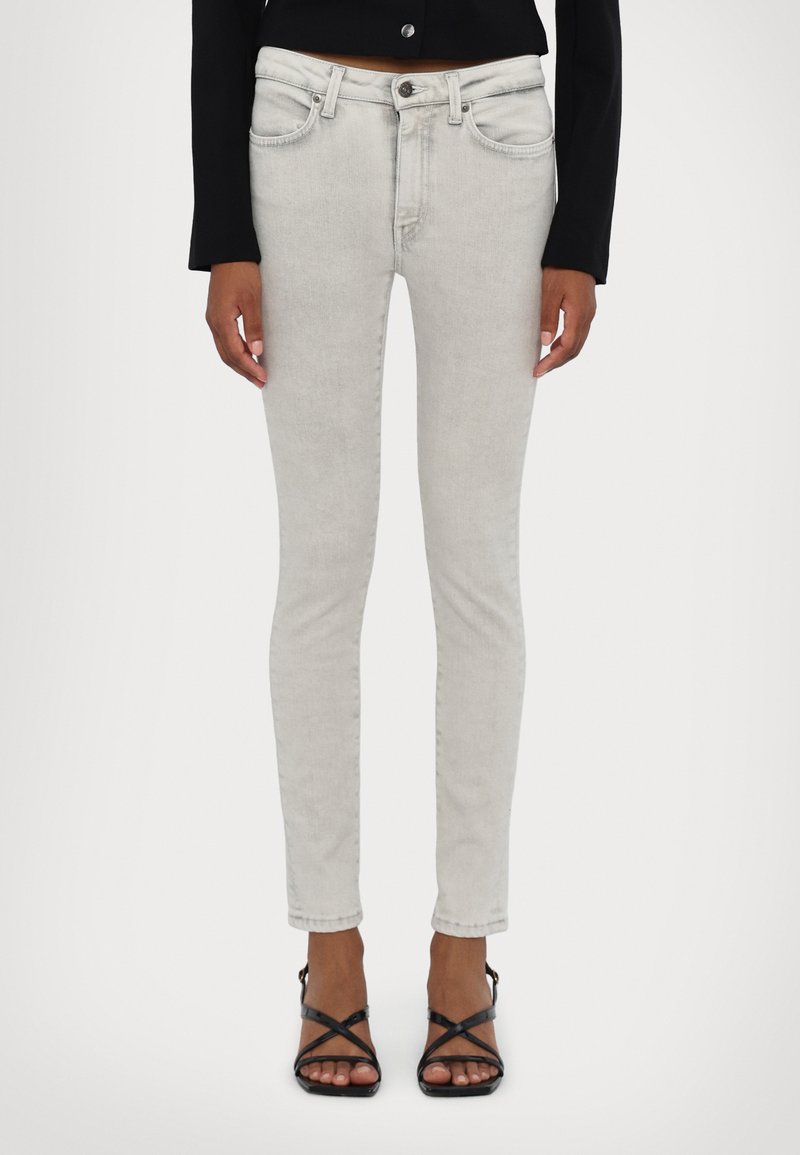 Jasnoszare dopasowane dżinsy z klasycznym pięciopocketowym wzorem, z zamkiem błyskawicznym i tonującym przeszyciem. W połączeniu z czarnymi, paskowymi szpilkami.