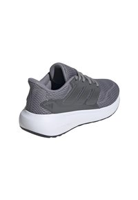 Zapatilla deportiva gris con parte superior de malla texturizada, cuello acolchado y acentos en capas en gris. Presenta una media suela blanca y una suela exterior negra.