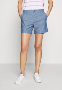 Lichtblauwe chambray shorts met een knoopsluiting, zijzakken en een relaxed fit, gecombineerd met witte sneakers.