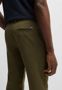 Herrbyxor i olivgrön färg med slim fit, sidofickor och bakfickor med en svart "BOSS"-logotyp. Slät tygstruktur.
