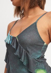 Dark adjustable-strap dress featuring tiered ruffles and a textured pattern with shades of green and black, highlighting a fluid design.