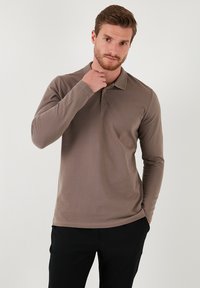 Camisa polo de manga larga, color marrón, con cuello, hecha de tela suave. Presenta un diseño ajustado con costuras sutiles y un dobladillo recto.