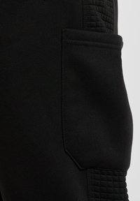 Svart joggebukse med teksturerte sidestykker og en sidelomme, laget av et mykt, elastisk stoff.