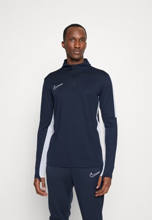 Granatowa sportowa bluzka z długim rękawem i zamkiem, z białymi bocznymi panelami oraz logo Nike na piersi. Gładki, elastyczny materiał.