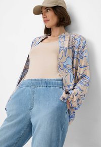 Chemise légère à motifs floraux en beige et bleu, associée à un débardeur beige et un pantalon en denim bleu clair ample.
