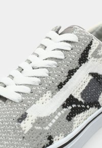 Grey camouflage sneaker with a textured knit upper, white laces, and contrasting accents in black and darker grey. Flat rubber sole.