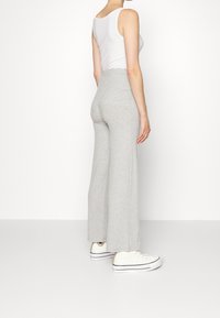 Grå ribbade vida byxor med hög midja, tillsammans med vita sneakers. Tyget har ett strukturerat mönster och en mjuk yta.