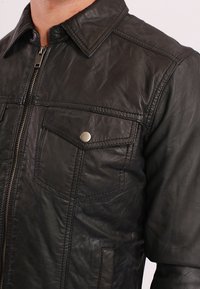 Černá kožená bunda s zipovým zapínáním, špičatým límcem, prsními kapsami se cvoky a texturovaným povrchem.