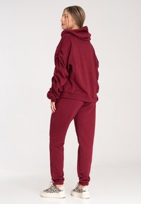 Bordowa bluza z kapturem, z bufkami i regulowanym kapturem, w komplecie ze spodniami dresowymi w tym samym kolorze. Miękka tkanina z elastycznymi mankietami i bocznymi kieszeniami.