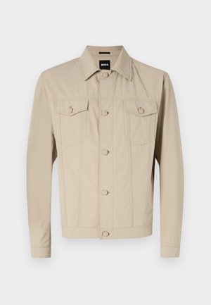 Beige farkkutakki, jossa on klassinen kaulus, etulukko napilla ja kaksi rintataskua; siinä on sauman yksityiskohtia ja pitkät hihat.