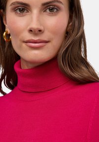 Dopasowany sweter z golfem w jasnoróżowej dzianinie, z żebrowanym kołnierzem i gładką fakturą, z widocznymi detalami szwów.