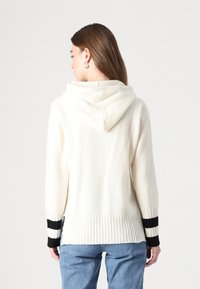 Svetrová mikina v krémovej pletenine, so zvonivými čierno-bielymi pruhmi na rukávoch a rebrovaným lemom. Mäkkučký povrch, uvoľnený strih.