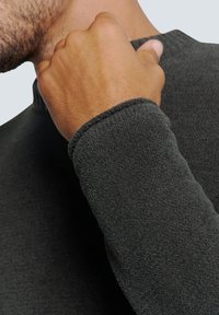 Dunkelgrauer Pullover mit hohem Kragen, aus weichem, strukturiertem Stoff und enganliegenden Ärmeln. Sichtbare Nähte entlang der Kanten.