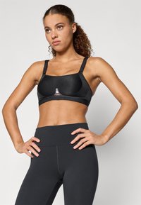 Sutien sport negru cu cupe modelate, bretele ajustabile și un logo la centru. Asortat cu colanți negri cu talie înaltă. Textură netedă.