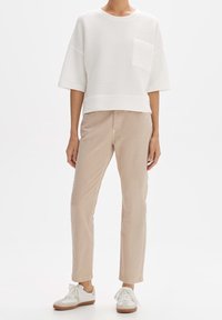 Suéter blanco corto con un diseño texturizado y mangas cortas, combinado con pantalones rectos beige y zapatillas blancas con acentos marrones.