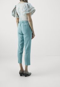 Vaaleansiniset pellavahousut, joissa on kapeneva lahje, yhdistettynä kukkakuosisella puserolla, jossa on puffihihat ja aaltoilevat reunat.