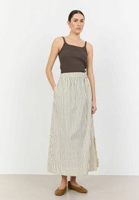 Brauner gerippter Tanktop, kombiniert mit einem langen, beige gestreifen Rock mit gerafftem Bund und Seitentaschen. Das Modell trägt braune Ballerinas.