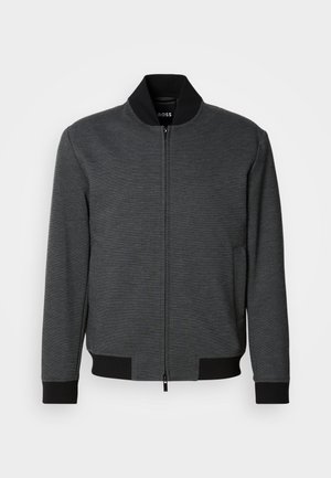 Σκούρο γκρι μπουφάν τύπου bomber με φερμουάρ, ριμπ γιακά και μανσέτες, λεία υφή και πλαϊνές τσέπες. Οριζόντια ραφή στο κάτω μέρος.