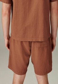 Short color marrone con texture e camicia coordinata realizzati in tessuto leggero. La camicia arriva fino alla vita e gli short presentano una tasca posteriore.