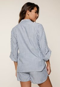 Conjunto de pijama ligero a rayas en azul y blanco, con un cuello abotonado, mangas arremangadas y una parte superior de corte holgado emparejada con pantalones cortos a juego.