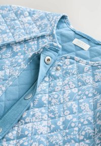 Giacca trapuntata blu con un motivo floreale bianco, dotata di bottoni a pressione e un'etichetta con la scritta "NEXT" all'interno del colletto.