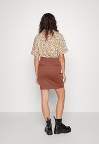 Blommig kortärmad skjorta med gröna, röda och vita mönster; bruna figurnära kjol; svarta snörstövletter med tjocka sula.