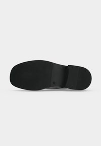 Semelle de chaussure noire avec texture rainurée au talon et à l'avant, section centrale lisse, sur fond blanc uni.
