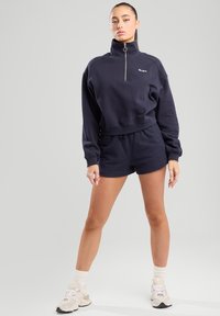 Navy cropped sweatshirt with high collar and zip detail, paired with matching navy shorts. Soft fabric texture, casual design.