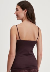 Bordeaux tanktop met dunne bandjes, voorzien van een gladde textuur en een ronde halslijn, gedetailleerd met delicate stiksels langs de randen.