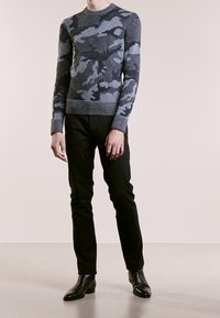 Grå camouflagemönstrad stickad tröja med rund halsringning, i kombination med åtsittande svarta byxor och svarta ankelstövlar, som visar en jämn textur.