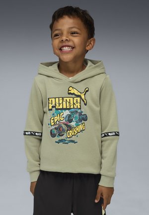 Lächelnder Junge, der einen hellgrünen Puma-Hoodie mit Monstertruck-Grafik und dem Text "Epic Crushing" trägt, kombiniert mit schwarzen Hosen, steht vor einem grauen Hintergrund.