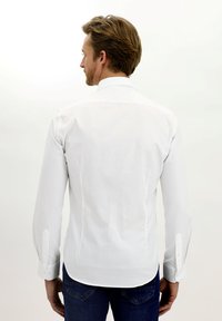 Camicia bianca con colletto button-up, maniche lunghe, vestibilità sartoriale e orlo dritto. Caratterizzata da un semplice design dei polsini e uno stile pulito e minimalista.