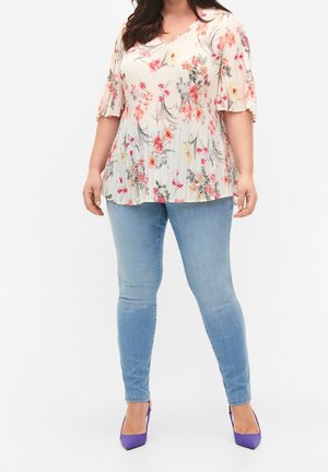 Haut à imprimé floral avec texture plissée, manches courtes et flottantes, et décolleté en V. Porté avec un jean skinny bleu clair et des talons hauts violets.