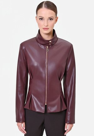 Donna che indossa una giacca di pelle aderente e lucida color bordeaux con collo alto e zip dorata, abbinata a pantaloni neri.