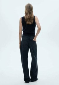 Czarne jeansy z wysokim stanem i szerokimi nogawkami o gładkiej fakturze, z dwoma tylnymi kieszeniami i luźnym krojem, zestawione z ciemnym, bezrękawnym topem.