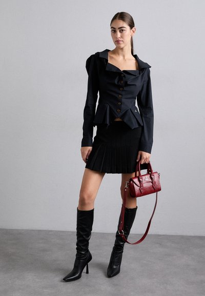 Blusa peplum preta com botões, saia plissada preta, botas pretas até ao joelho e uma pequena carteira de crocodilo vermelha.