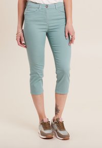 Pantaloni capri color turchese chiaro con una texture liscia, tasche frontali e chiusura con bottone. Abbinati a sneakers sportive multicolori.