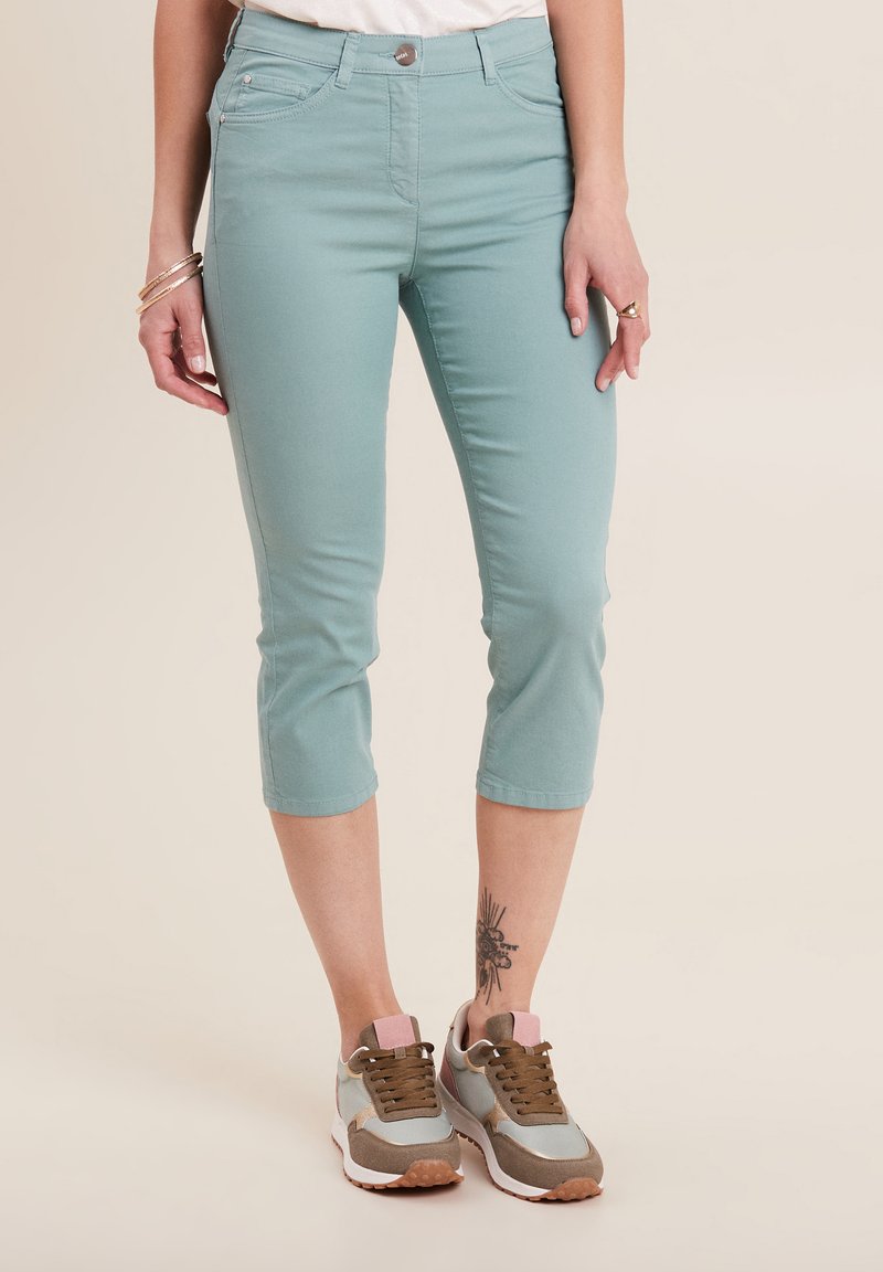 Pantaloni capri color turchese chiaro con una texture liscia, tasche frontali e chiusura con bottone. Abbinati a sneakers sportive multicolori.