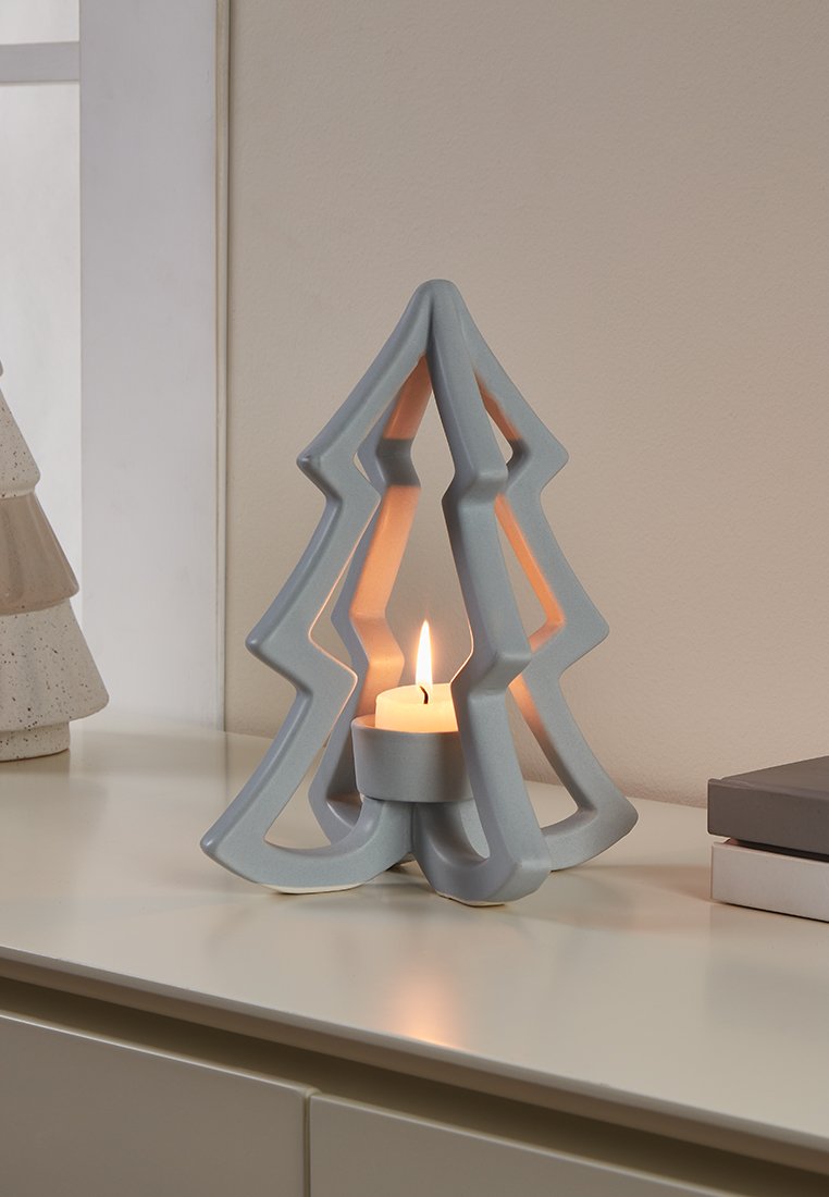 Grauer keramischer Kerzenhalter in Form eines Weihnachtsbaumes, mit einem zentralen Halter für eine weiße Kerze, der durchbrochene Designs für Licht aufweist.