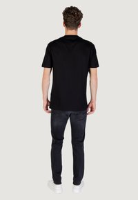 Camiseta negra de manga corta hecha de algodón, con un diseño clásico de cuello redondo, combinada con jeans oscuros y zapatos blancos.