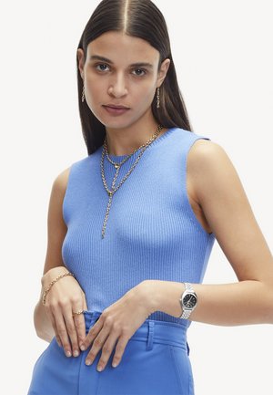 Haut sans manches côtelé bleu avec un col rond, associé à un bas bleu taille haute ajusté. Les bijoux comprennent des chaînes et des bracelets en or superposés.