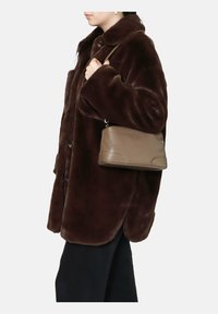 Cappotto in pelliccia sintetica marrone con colletto, vestibilità over e bottoni grandi; abbinato a una borsa in taupe testurizzato tenuta dalla persona.